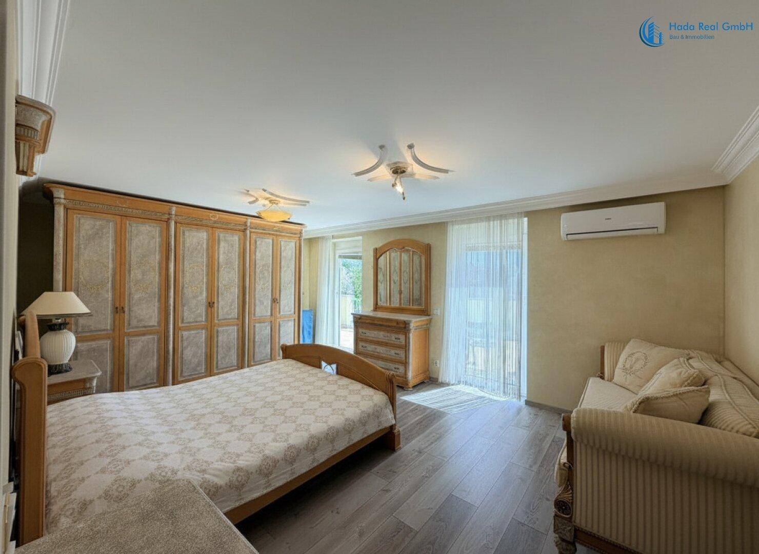 Geräumiges Schlafzimmer mit großem Kleiderschrank, Bett und Sofa, inklusive Klimaanlage und Holzboden.