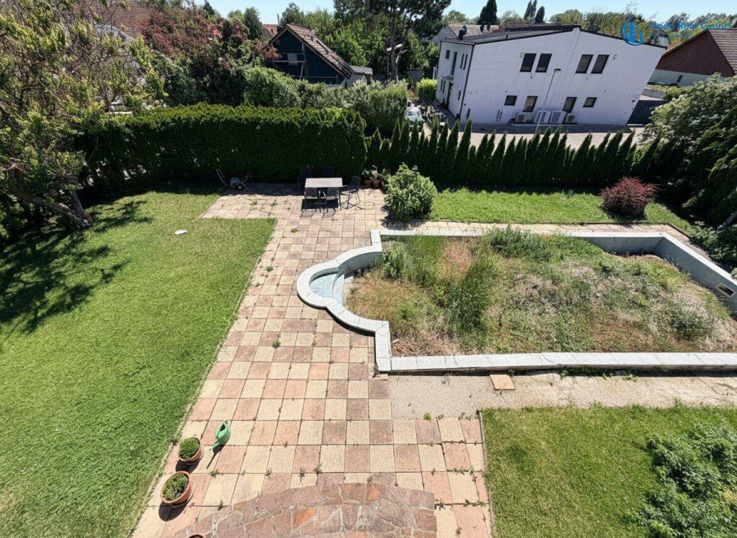 Vogelperspektive auf den Gartenbereich mit vernachlässigtem Pool und gepflasterten Wegen.