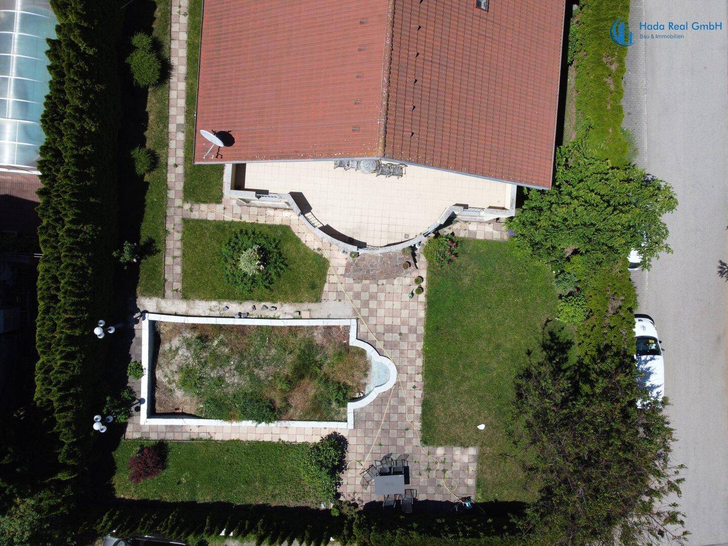 Luftaufnahme des hinteren Gartens mit großer Terrasse, Rasenflächen und Poolbereich.