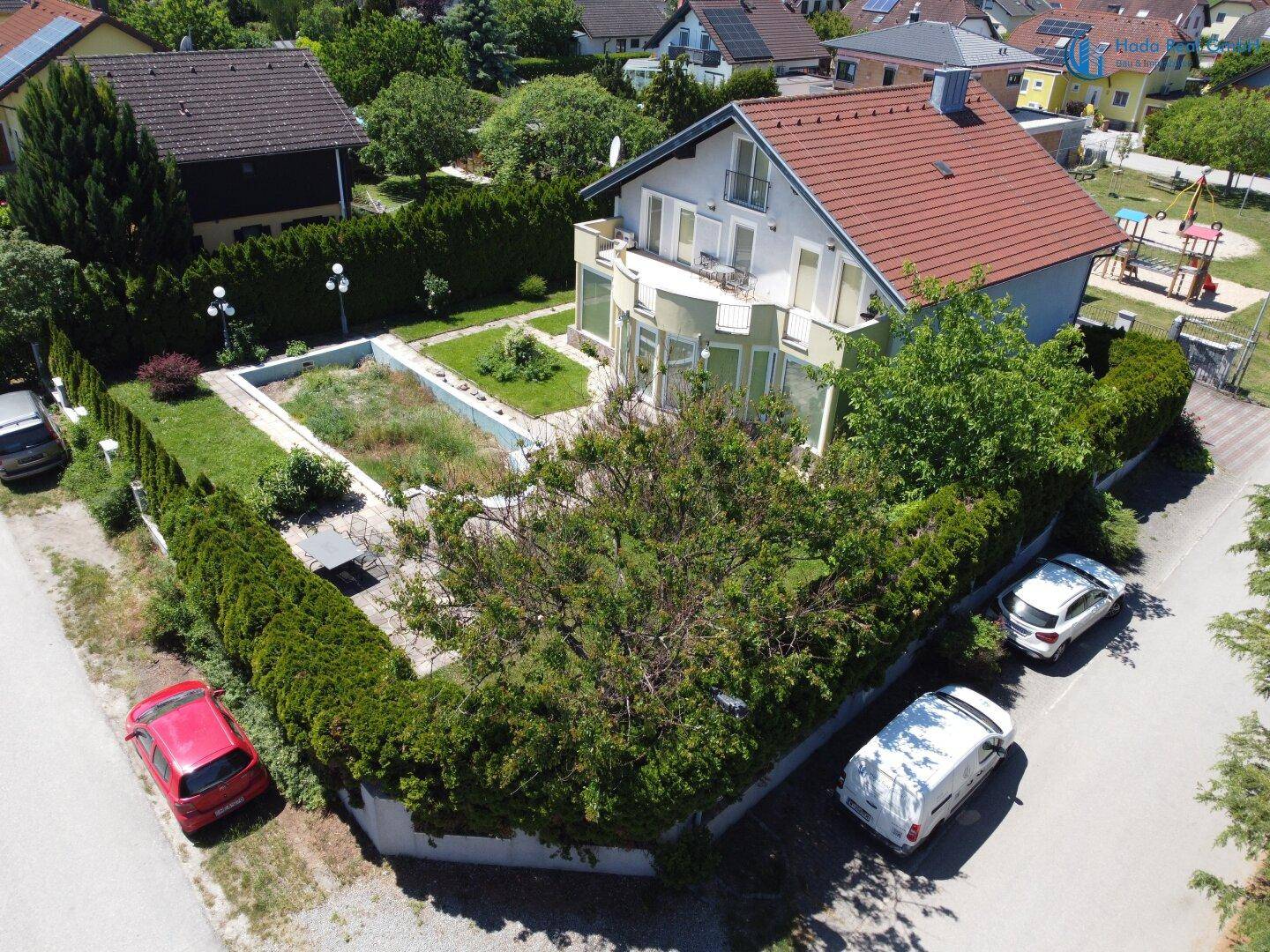 Weitläufige Luftaufnahme des Anwesens mit Garten, Hecken und angrenzender Straße.