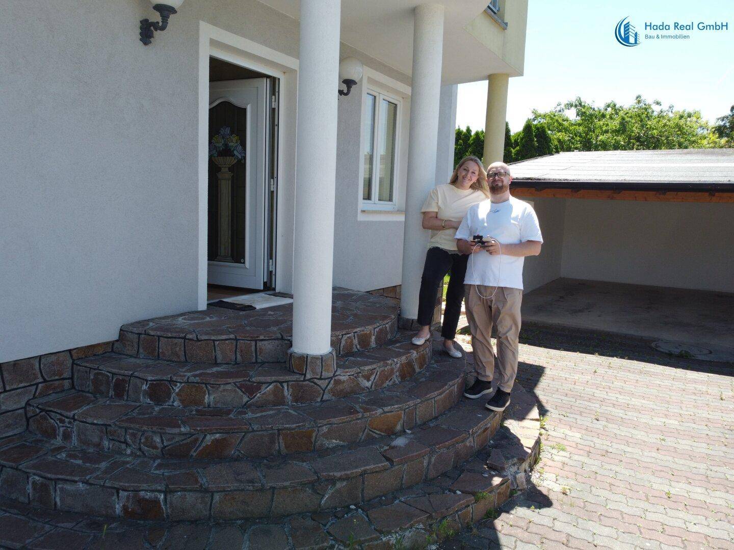 Eingangsbereich des Hauses mit geschwungener Steintreppe, Säulen und gepflasterter Auffahrt.