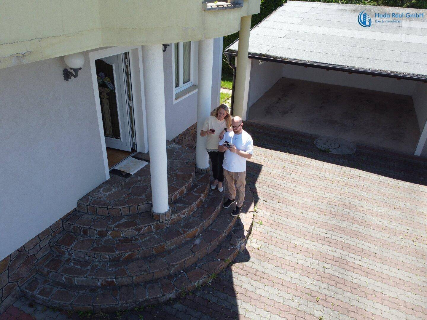 Eine Drohnenansicht zeigt den Eingangsbereich des Hauses mit Steintreppe und dem angrenzenden Carport.