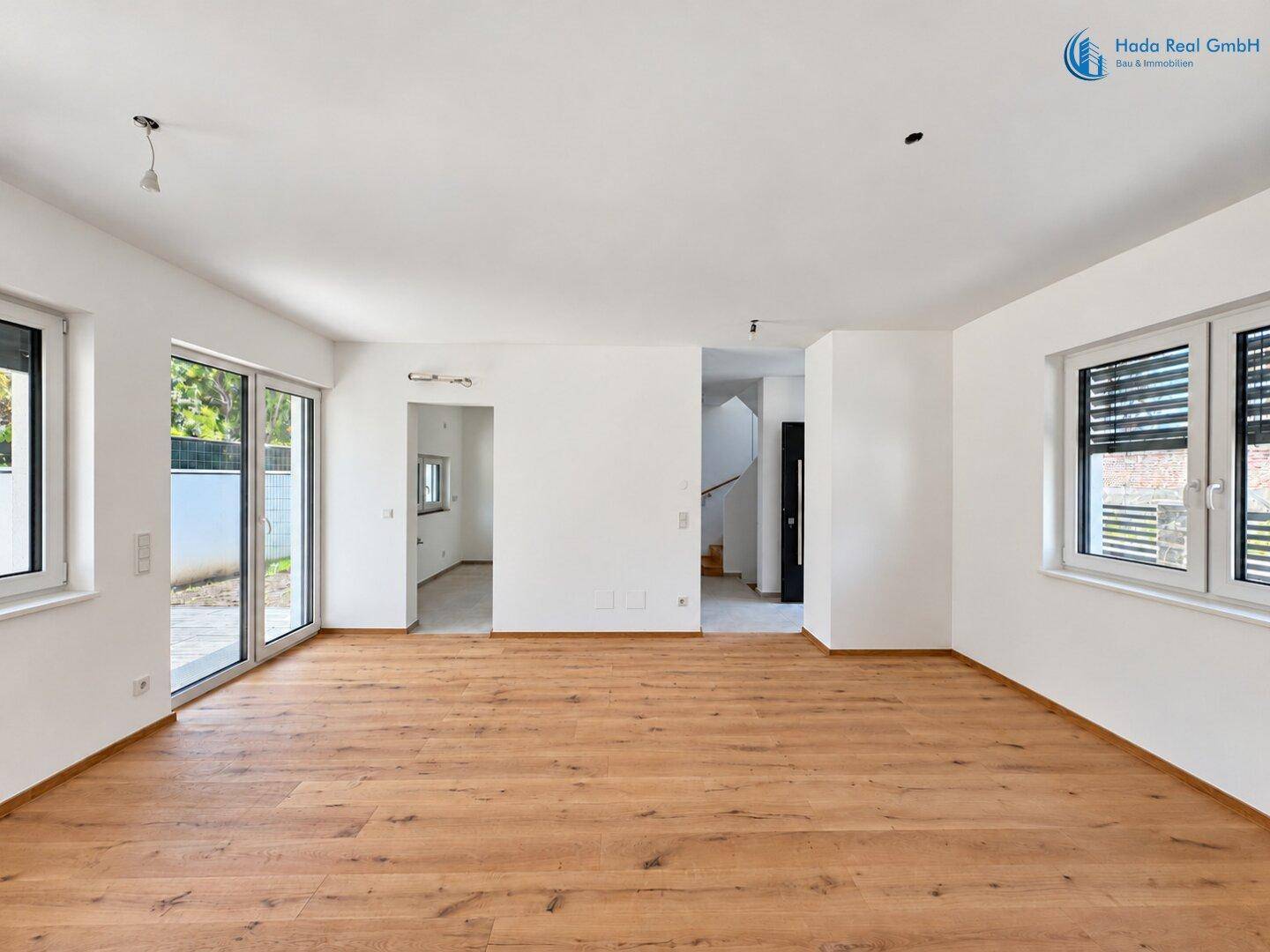Geräumiges, leeres Wohnzimmer mit Holzboden, großen Fenstern und Zugang zur Terrasse.