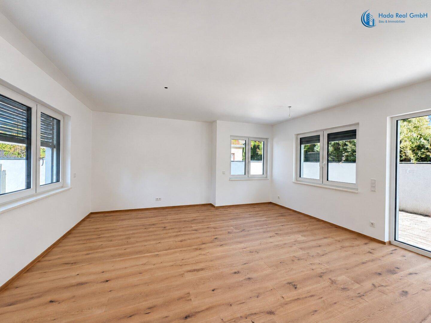 Helles Wohnzimmer mit Holzboden, vielen Fenstern und Rollläden, die einen Blick ins Grüne ermöglichen.