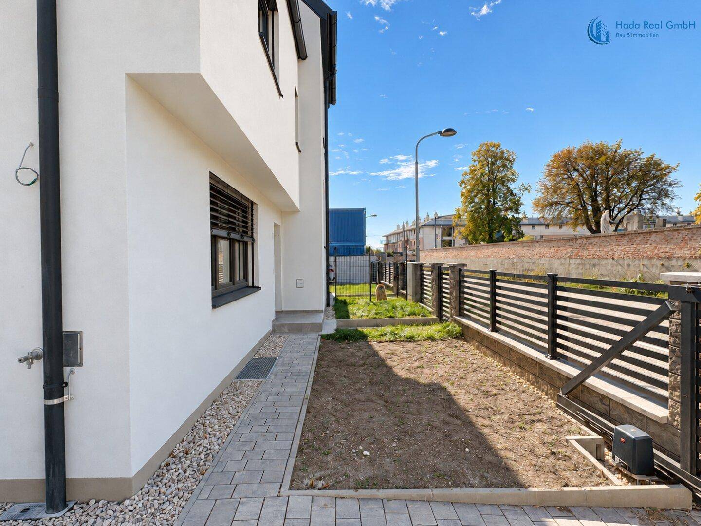 Seitenansicht des Hauses mit schmalem Gartenstreifen, gepflastertem Weg und Zaun.