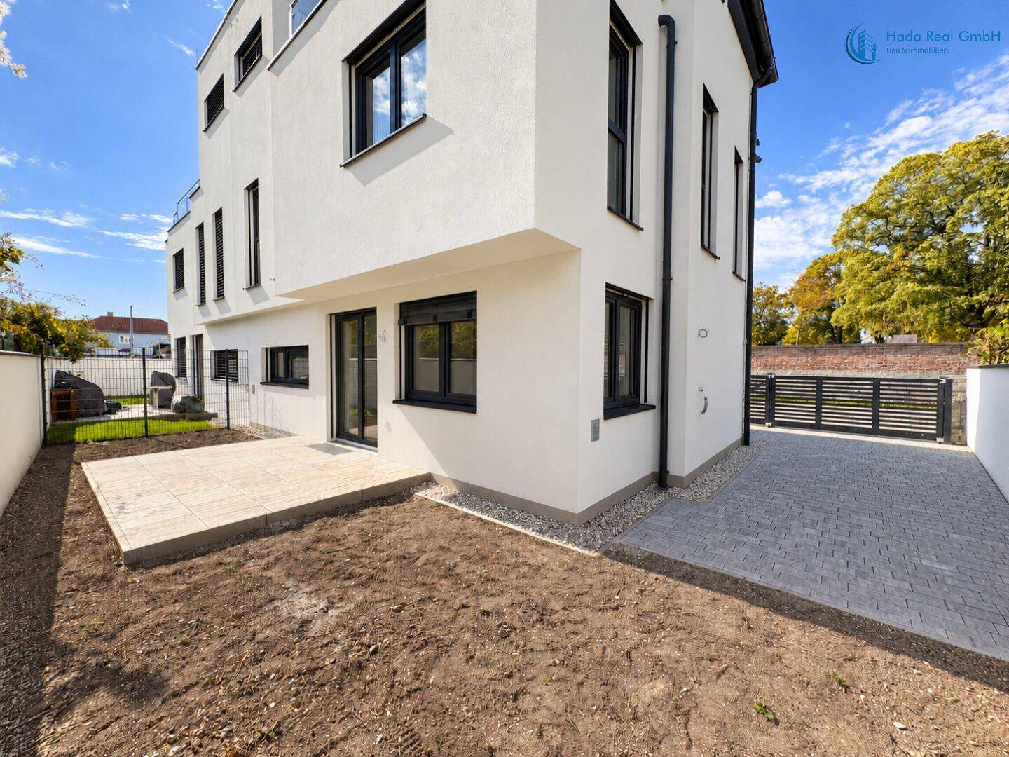 Hinterhof mit gepflasterter Terrasse und vorbereiteter Rasenfläche unter blauem Himmel.