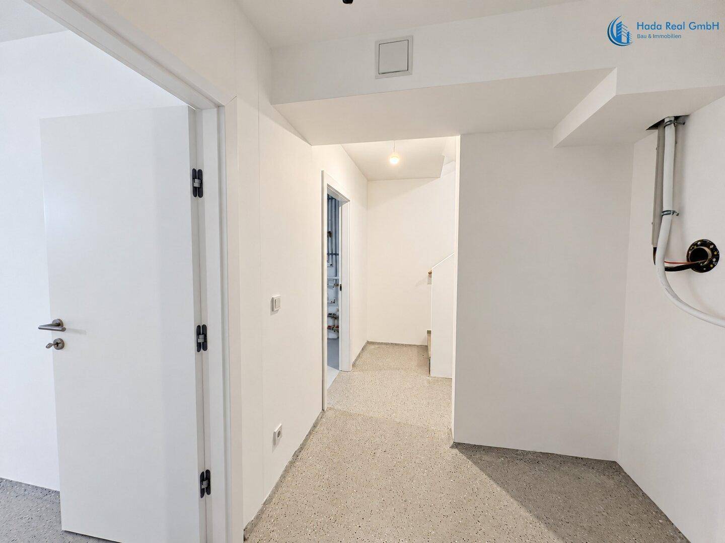 Kellerflur mit Zugang zu weiteren Räumen und sichtbaren Installationen an der Decke.