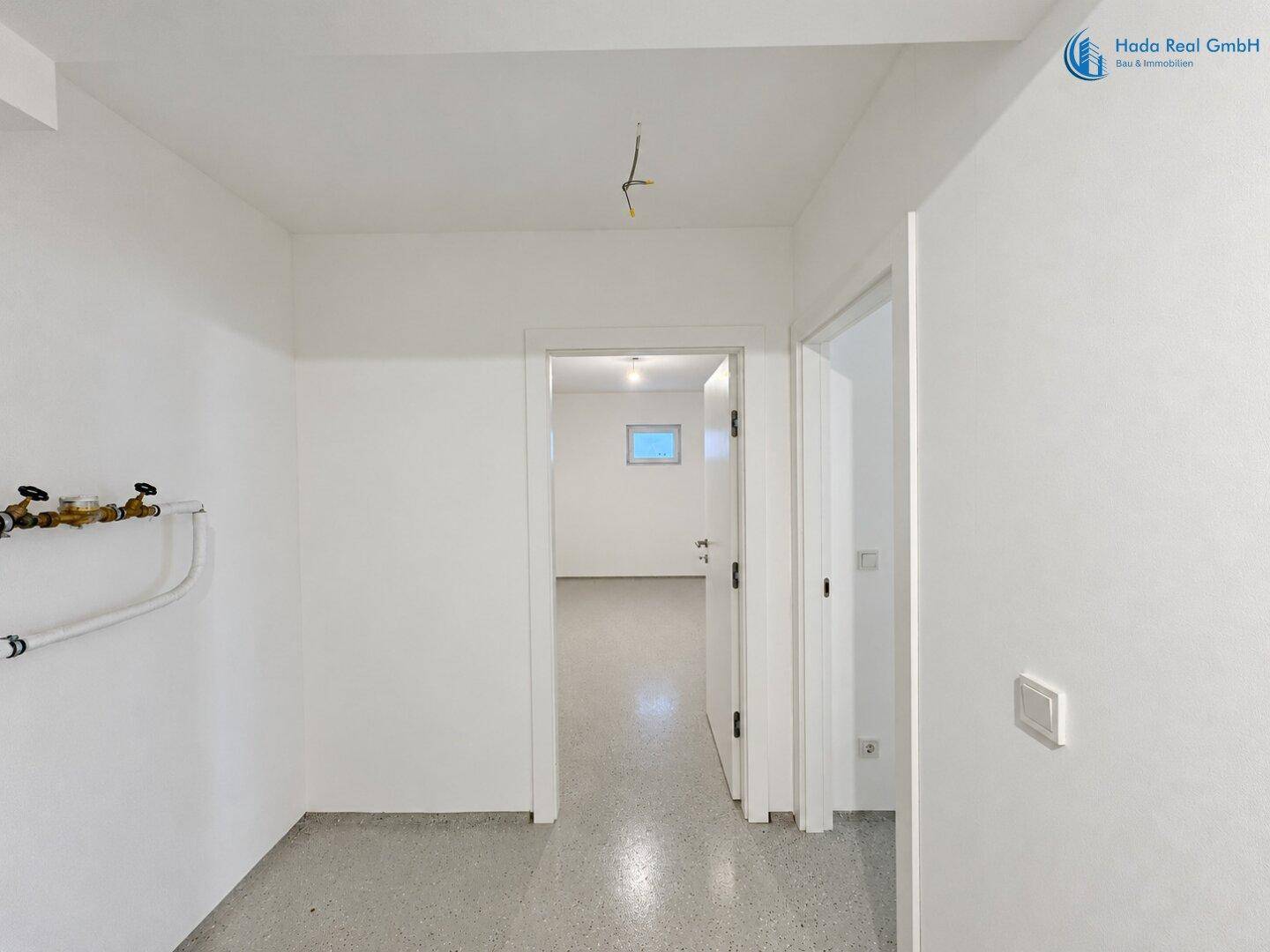 Kellerraum mit sichtbaren Leitungen und Zugang zu weiteren Bereichen, ideal als Abstellraum.