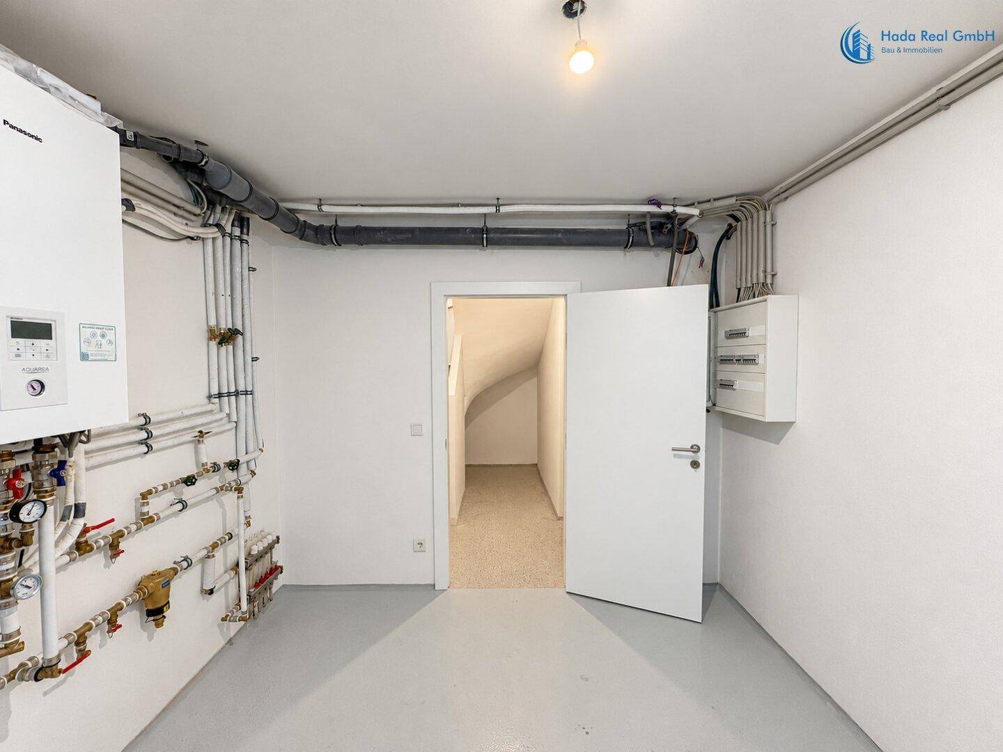 Heizungsraum mit moderner Technik, vielen Rohren und Zugang zum Treppenhaus.