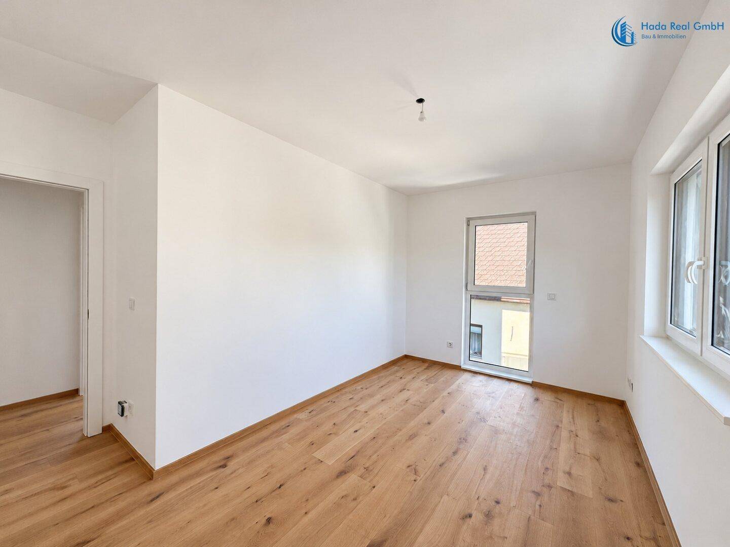 Helles Schlafzimmer mit Holzboden und Zugang zu einem französischen Balkon.