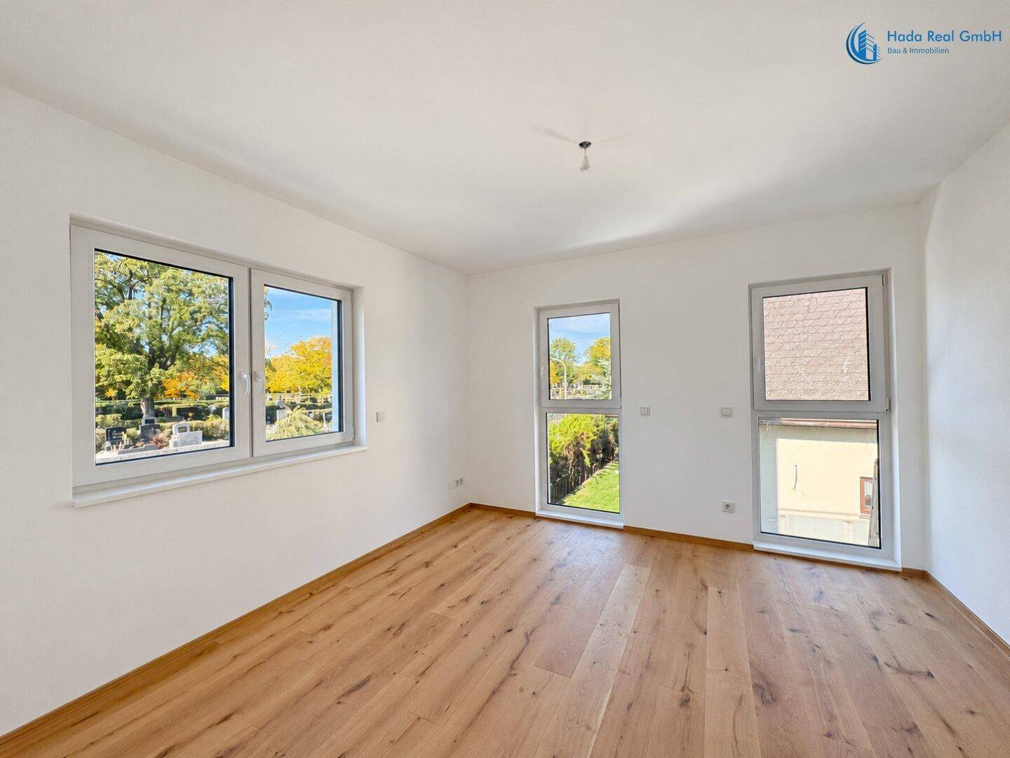Geräumiges Zimmer mit Holzboden und großen Fenstern, die viel Tageslicht hereinlassen.