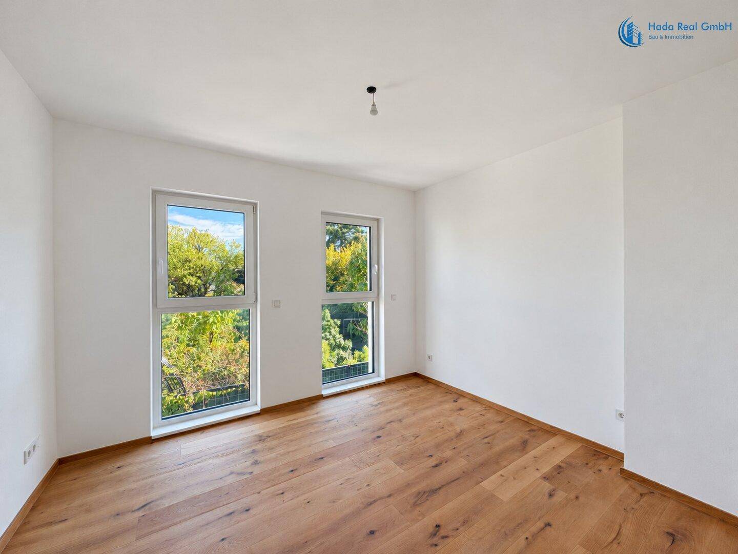 Ruhiges Zimmer mit Holzboden und zwei Fenstern, die einen angenehmen Ausblick ermöglichen.