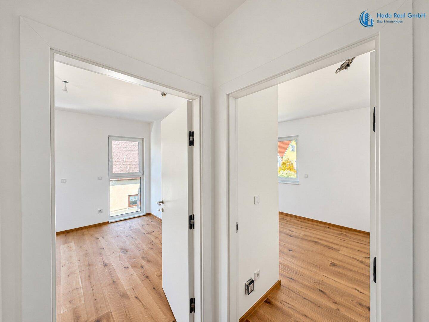 Blick vom Flur in zwei helle Zimmer mit Holzboden und großen Fenstern.