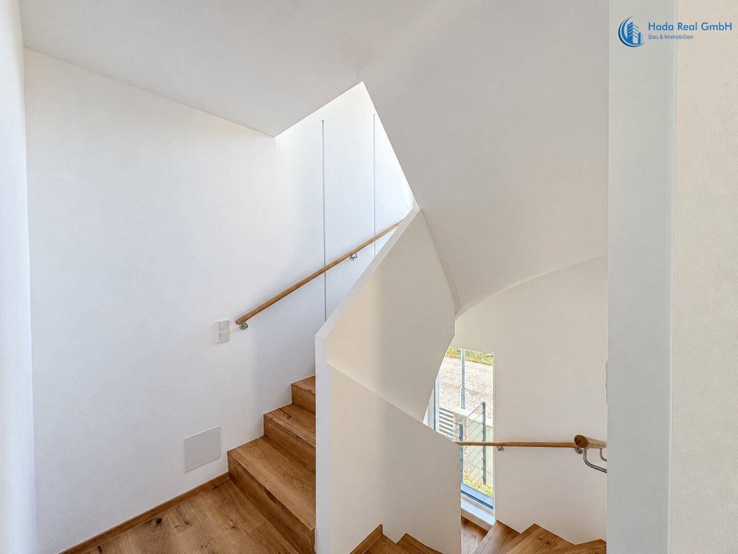 Moderner Treppenaufgang mit Holzstufen und großem Fenster, das viel Licht spendet.