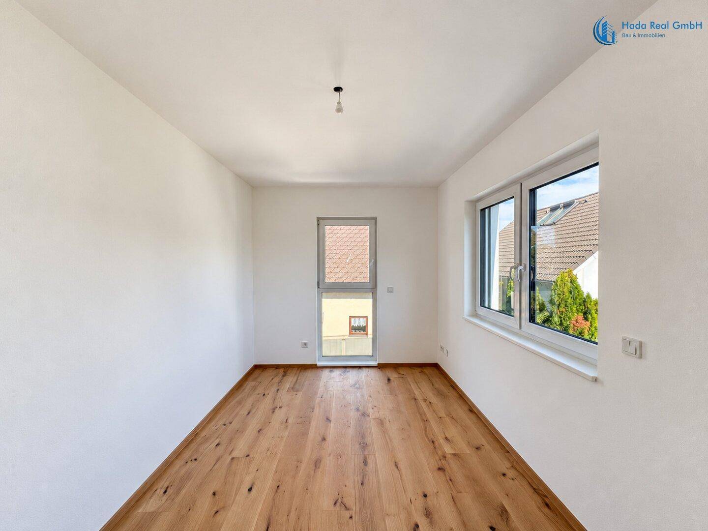 Freundliches Zimmer mit Holzboden und Fenster, das viel Tageslicht hereinlässt.