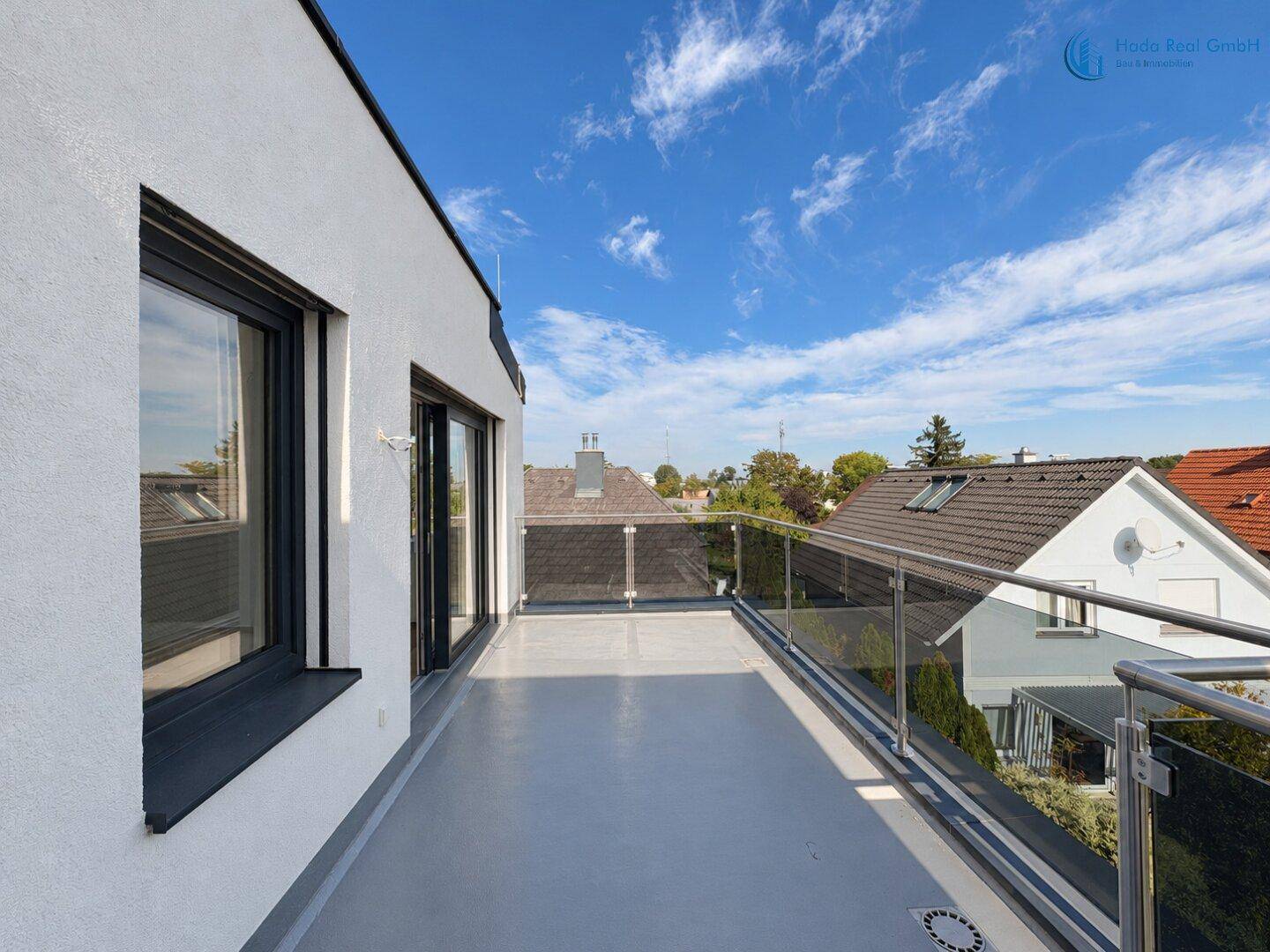 Geräumiger Balkon mit Glasgeländer und Blick auf die umliegenden Häuser und Bäume.