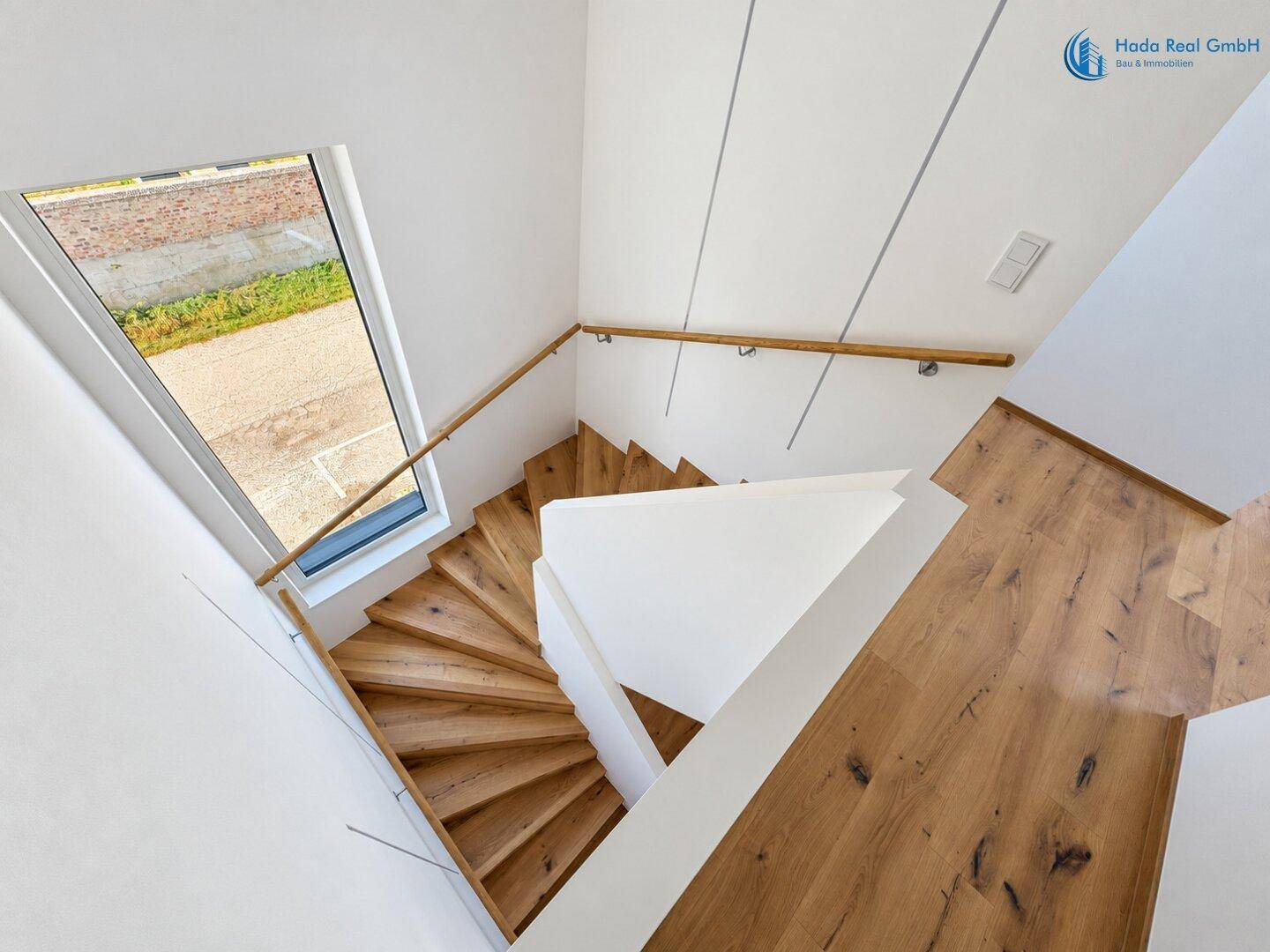 Helles Treppenhaus mit Holzstufen und modernem Geländer, das verschiedene Etagen miteinander verbindet.