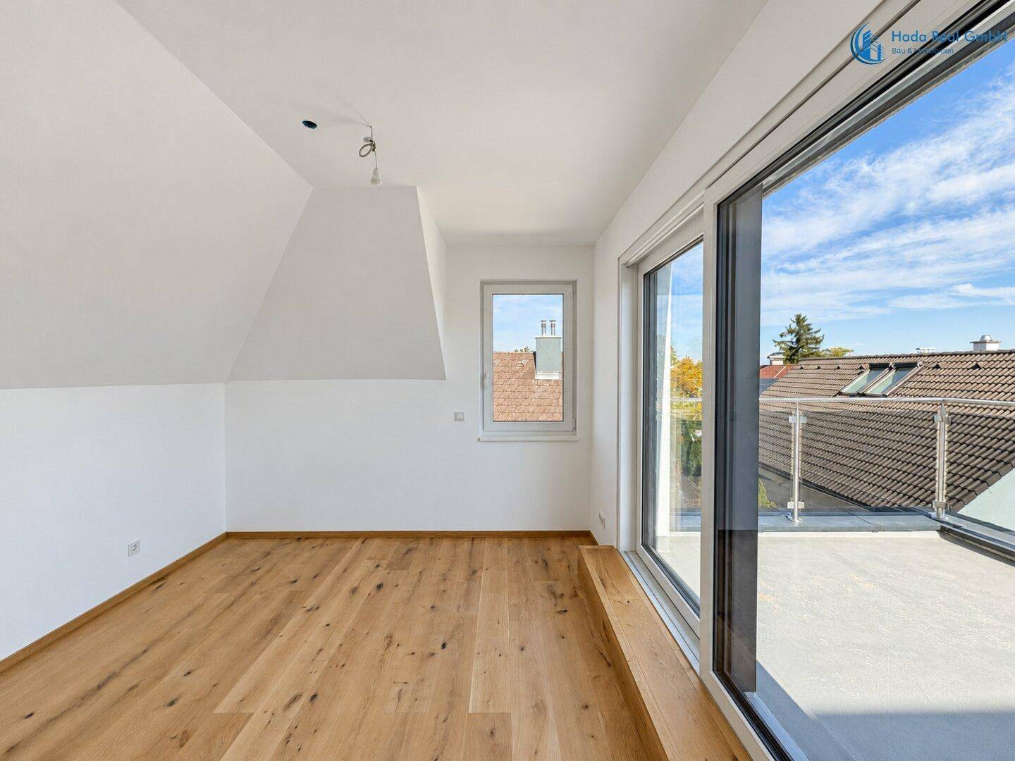 Heller Raum im Dachgeschoss mit Holzboden, großen Fenstern und Zugang zu einer Terrasse.