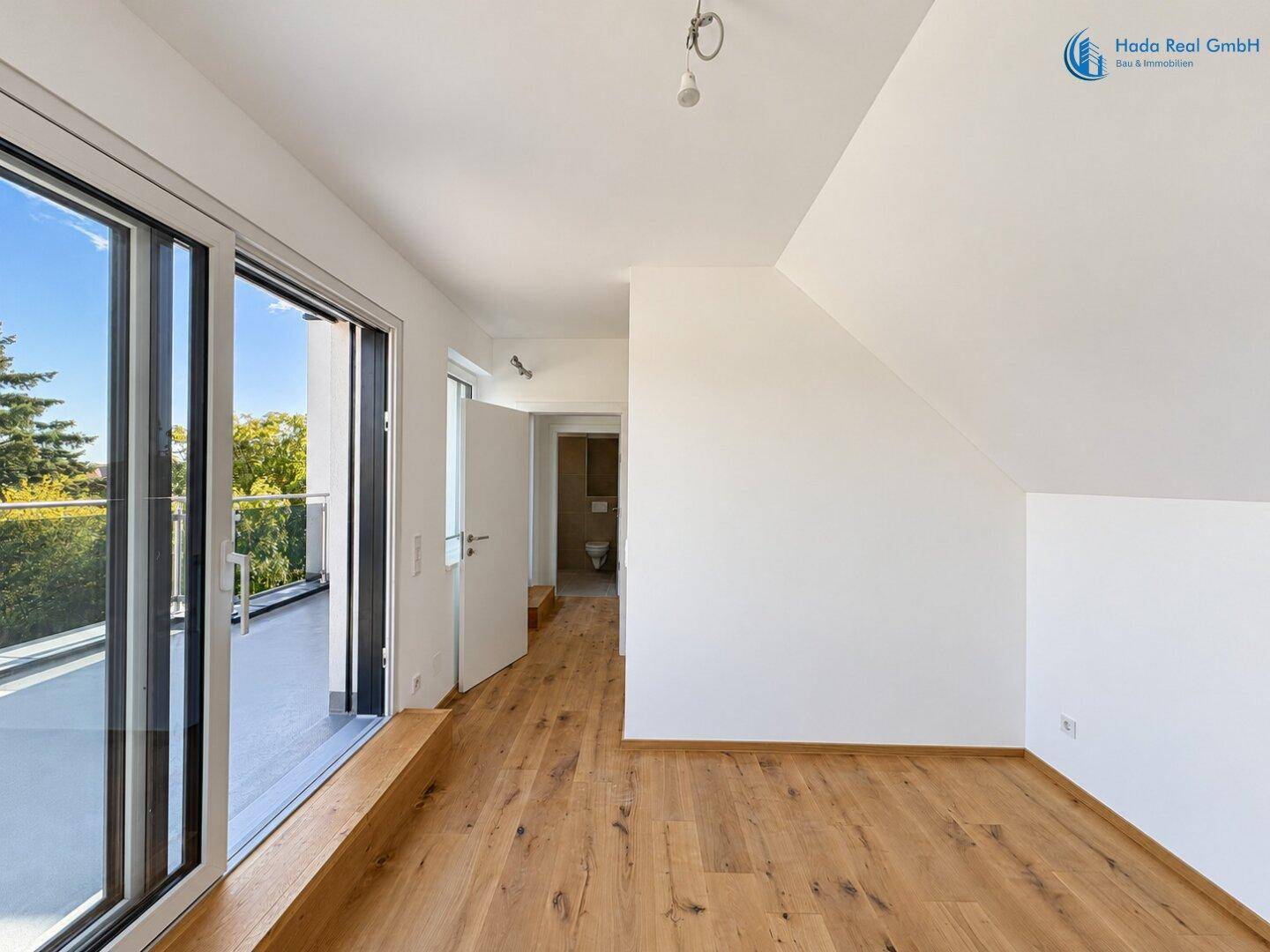 Lichtdurchfluteter Raum mit Holzboden, Dachschräge und direktem Zugang zur sonnigen Terrasse.