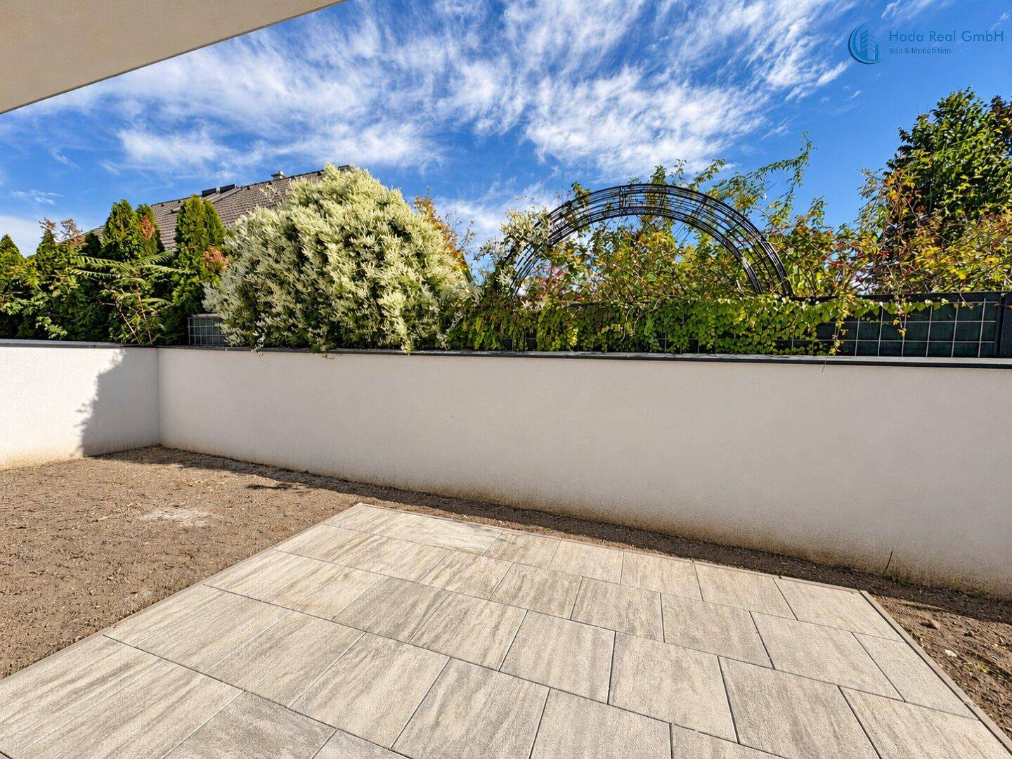 Neu angelegte Terrasse mit Pflastersteinen und angrenzendem Gartenbereich, umgeben von Grün.