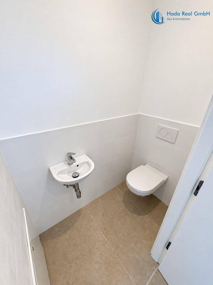 Modernes Gäste-WC mit wandhängender Toilette, kleinem Waschbecken und hellen Fliesen.