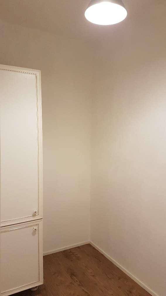 Ecke eines leeren Raumes mit weißem Schrank und Laminatboden, vielseitig nutzbar.