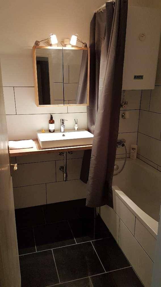 Badezimmer mit Waschbecken, Spiegelschrank und Badewanne mit Duschvorhang, auf dunklen Fliesen.