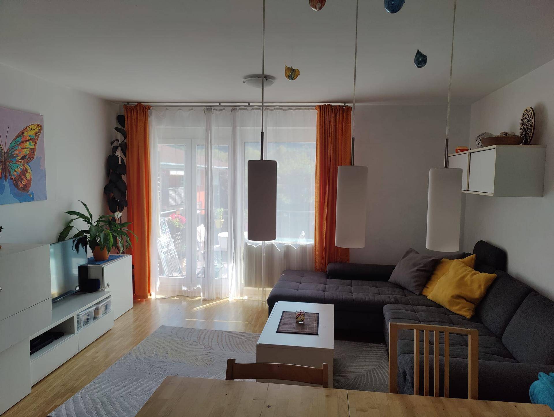 Helles Wohnzimmer mit modernem Sofa, Holzboden und Zugang zu einem Balkon.