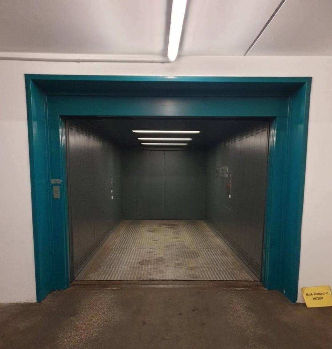 Geräumiger Lastenaufzug mit Metalltüren und blauer Umrandung, ausgestattet mit künstlicher Beleuchtung.