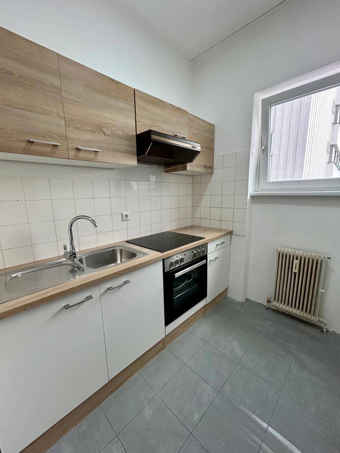 Kleine Küche mit weißen Unterschränken, Holzakzenten, Induktionskochfeld und Fliesenboden.