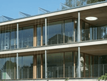 Moderne Gebäudefassade mit großen Glasfronten, Balkonen und einer markanten Dachkonstruktion.