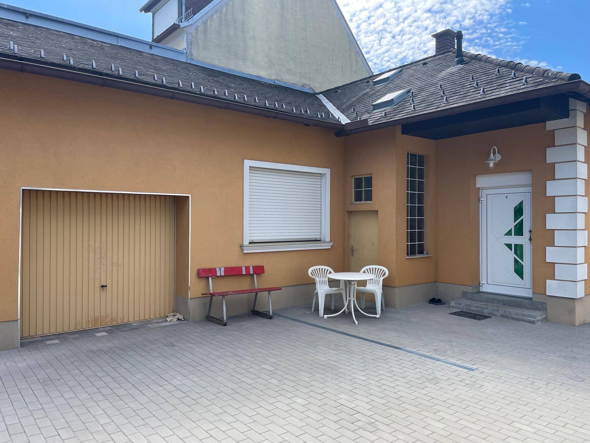 Hausfassade in Ockerfarbe mit Garagentor, Eingangstür und gepflastertem Vorplatz.