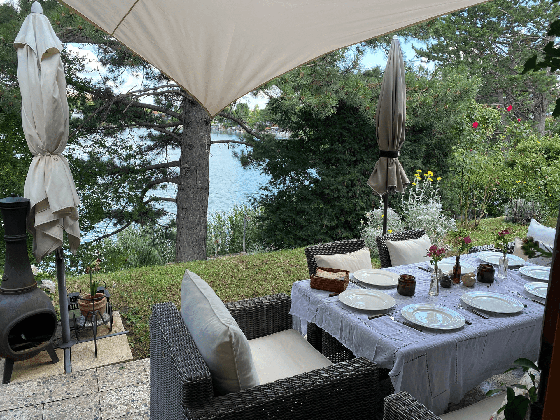 Gedeckter Esstisch auf der Terrasse mit Blick auf den See und umgeben von üppigem Grün.