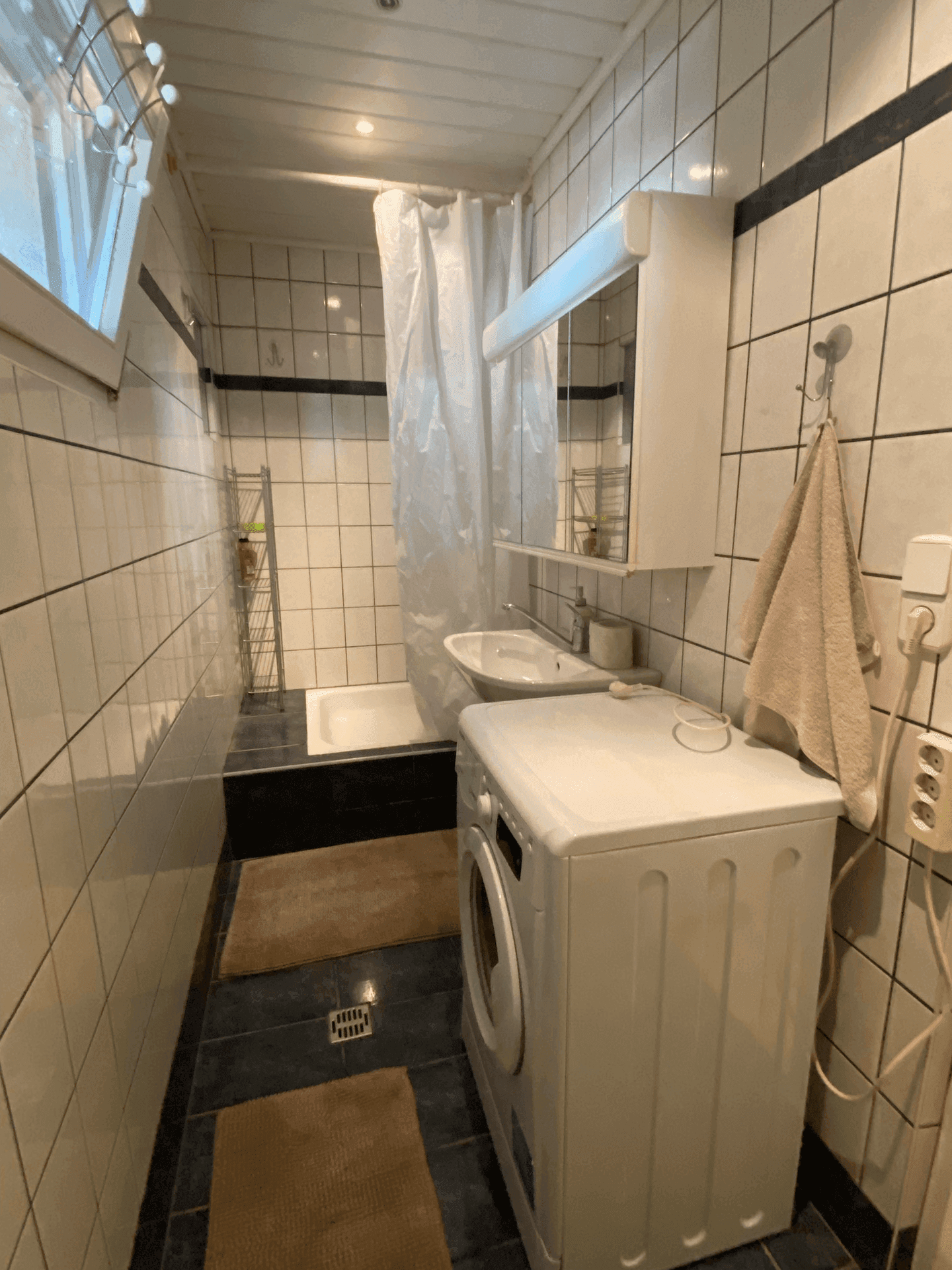 Schlichtes Badezimmer mit Badewanne, Waschmaschine und weiß-schwarzen Fliesen.