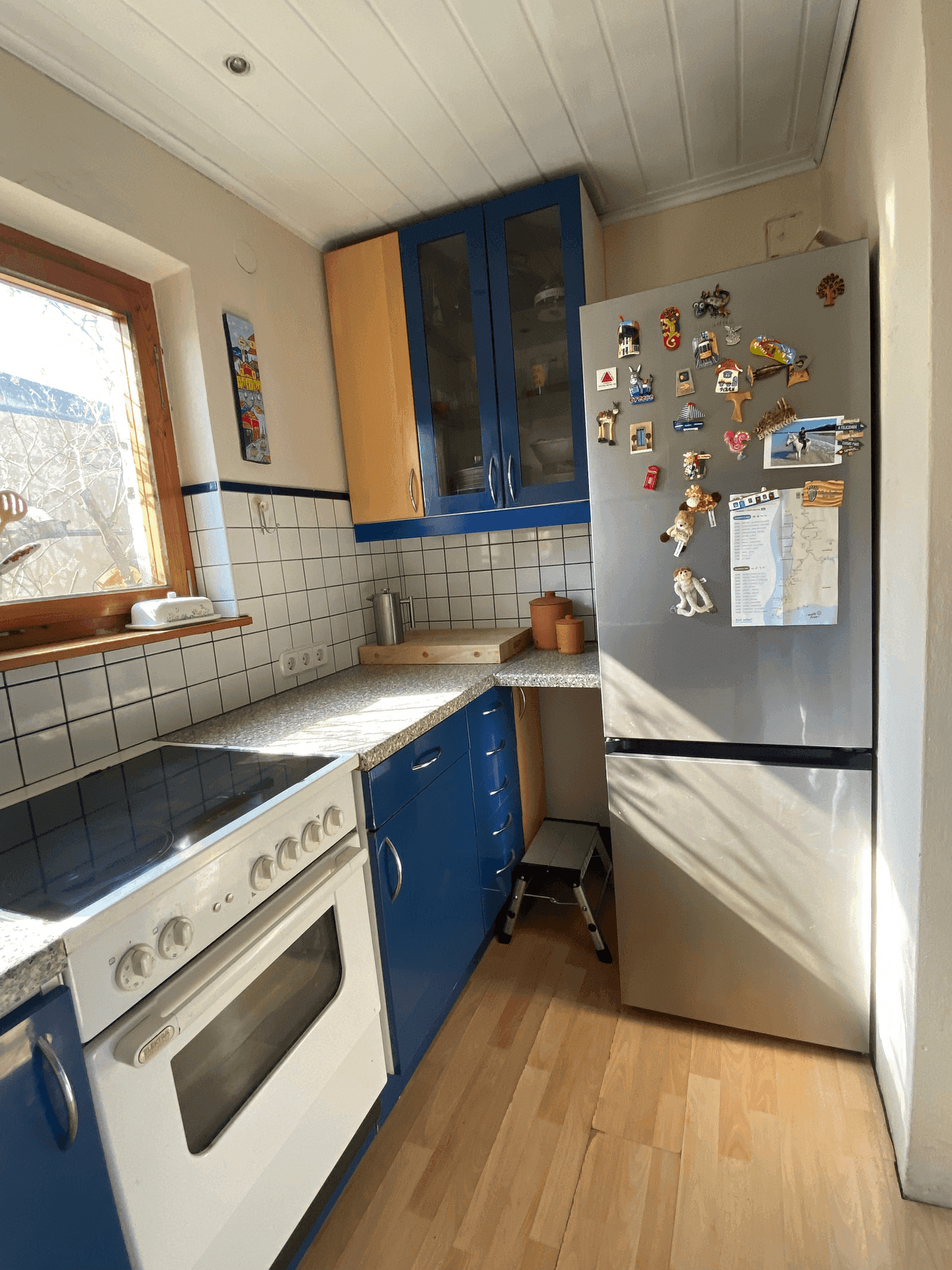 Funktionale Küche mit blauen Unterschränken, Kühlschrank und Induktionskochfeld, hell und sauber.