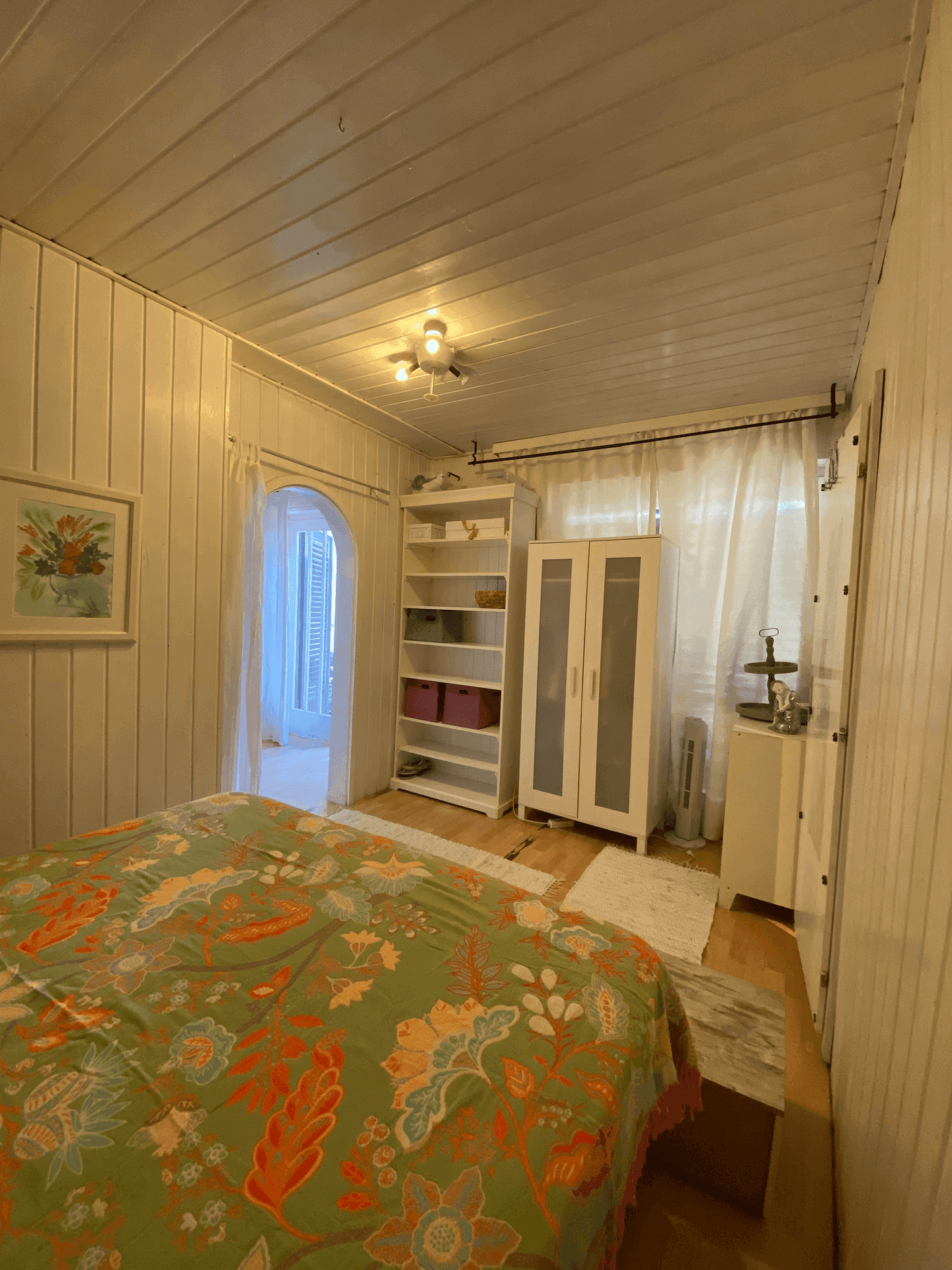 Helles Schlafzimmer mit weiß getäfelten Wänden, Schrank und Blick nach draußen.