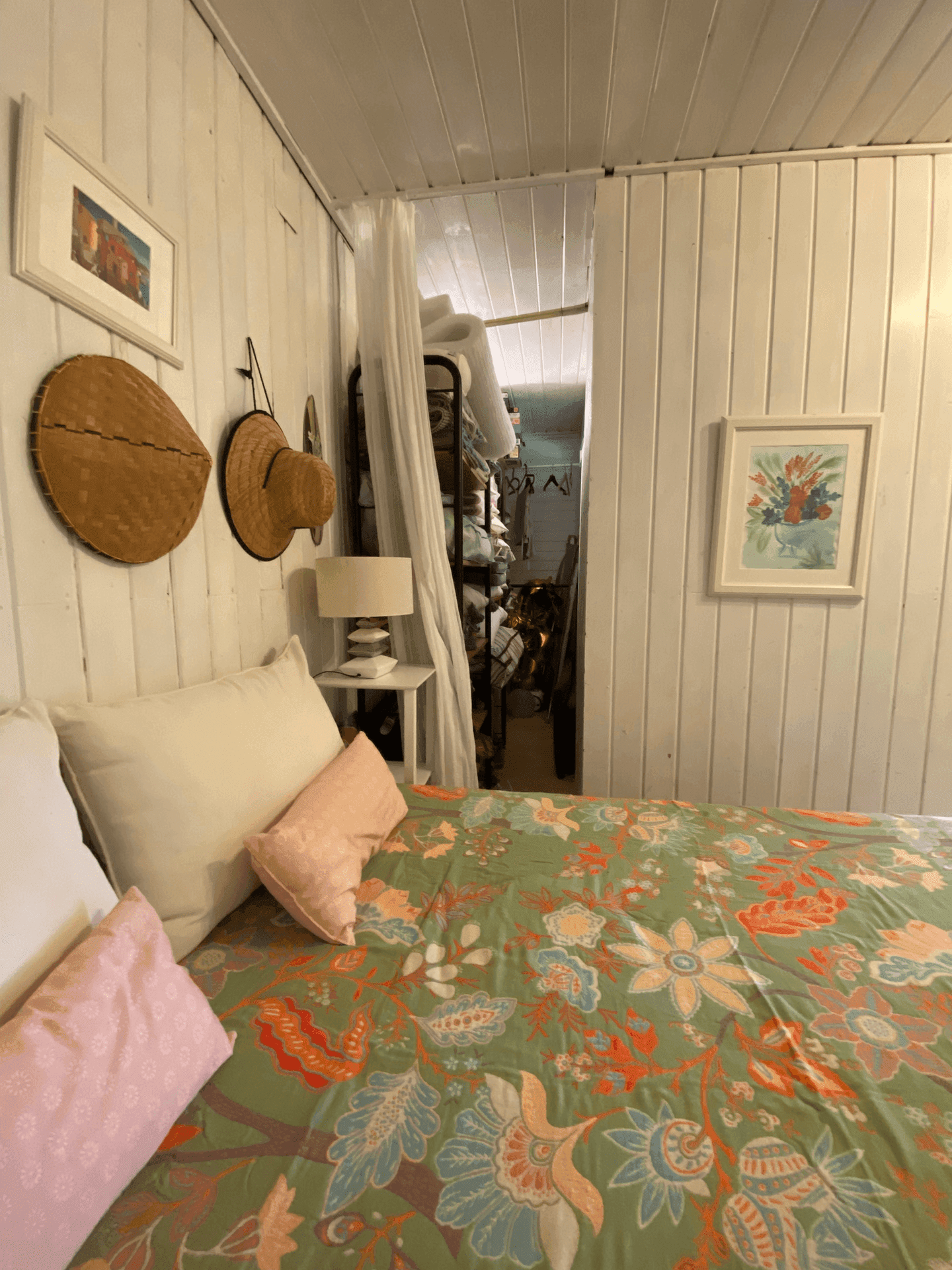 Schlafzimmer mit floraler Bettwäsche und Blick in einen angrenzenden Abstellraum.