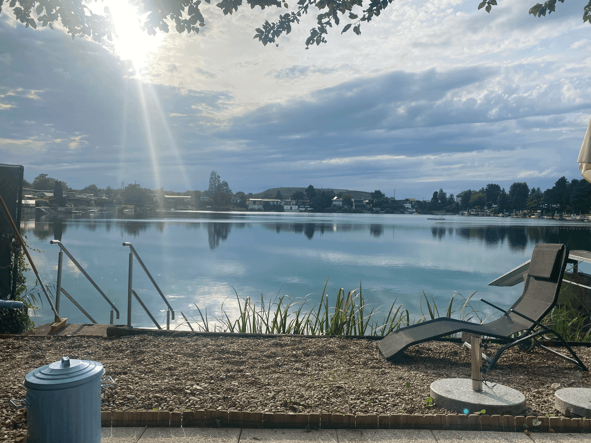 Sonniger Außenbereich am Seeufer mit Liegestuhl und direktem Zugang zum Wasser.