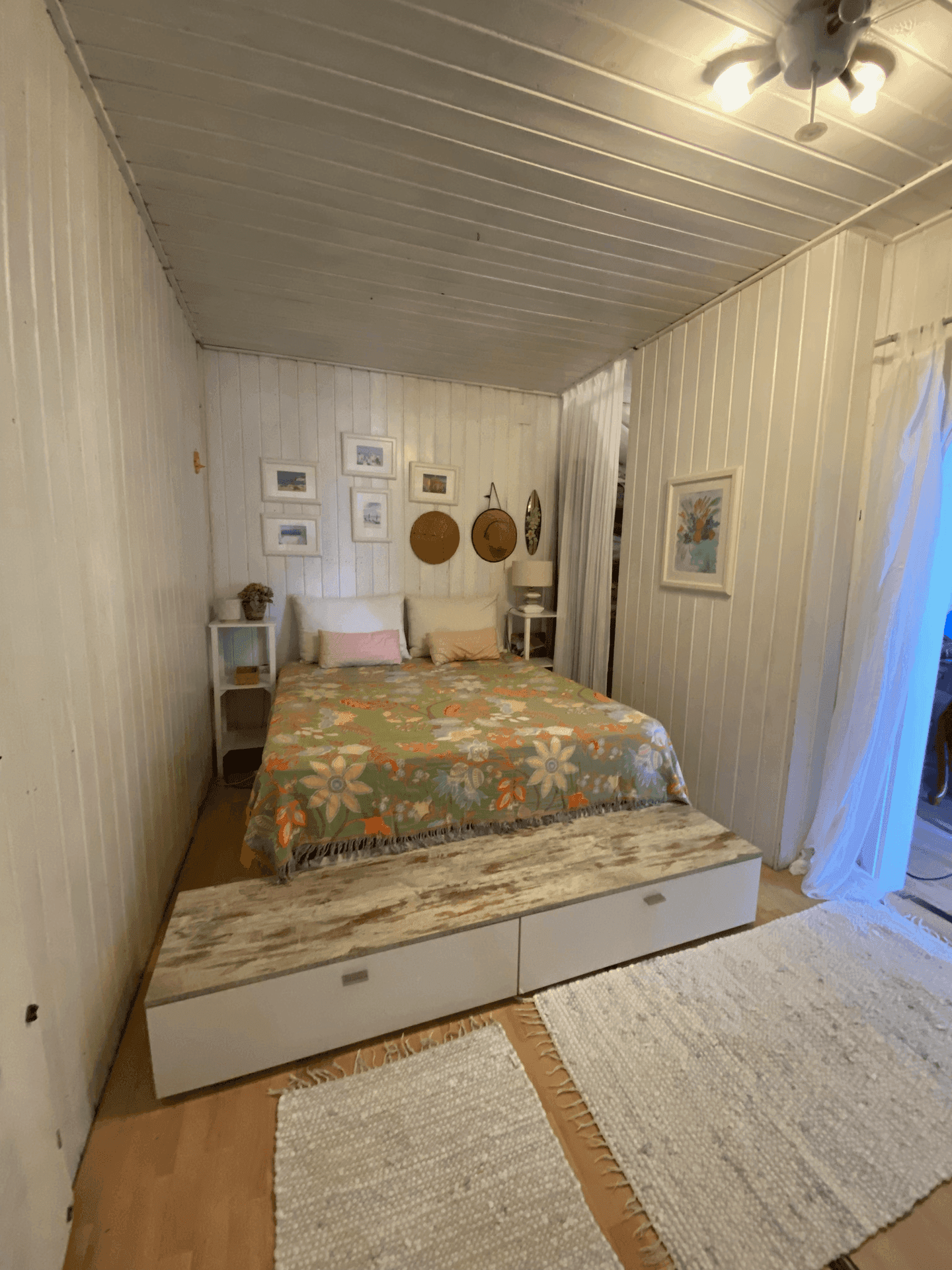 Gemütliches Schlafzimmer mit Holzbettgestell, floraler Bettwäsche und weiß getäfelten Wänden.