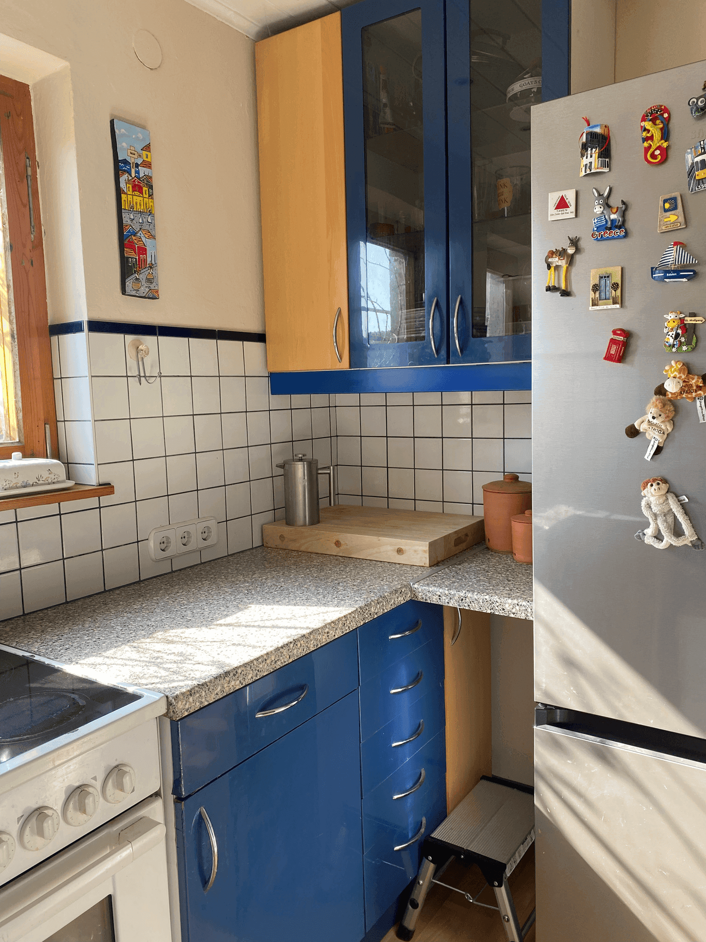 Helle Küche mit blauen und holzfarbenen Schränken, Kühlschrank und gefliester Arbeitsplatte.