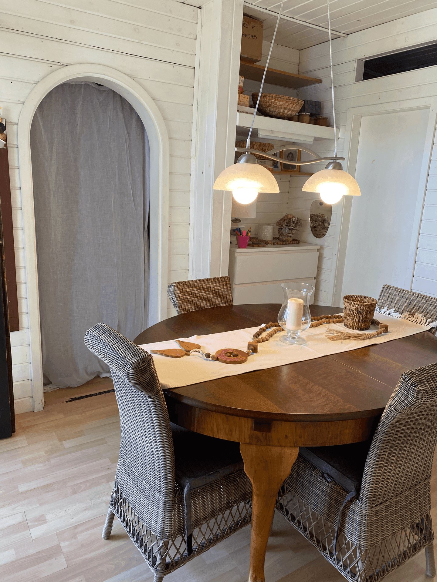 Rustikaler Essbereich mit Holztisch und Korbstühlen, beleuchtet von einer Deckenlampe.