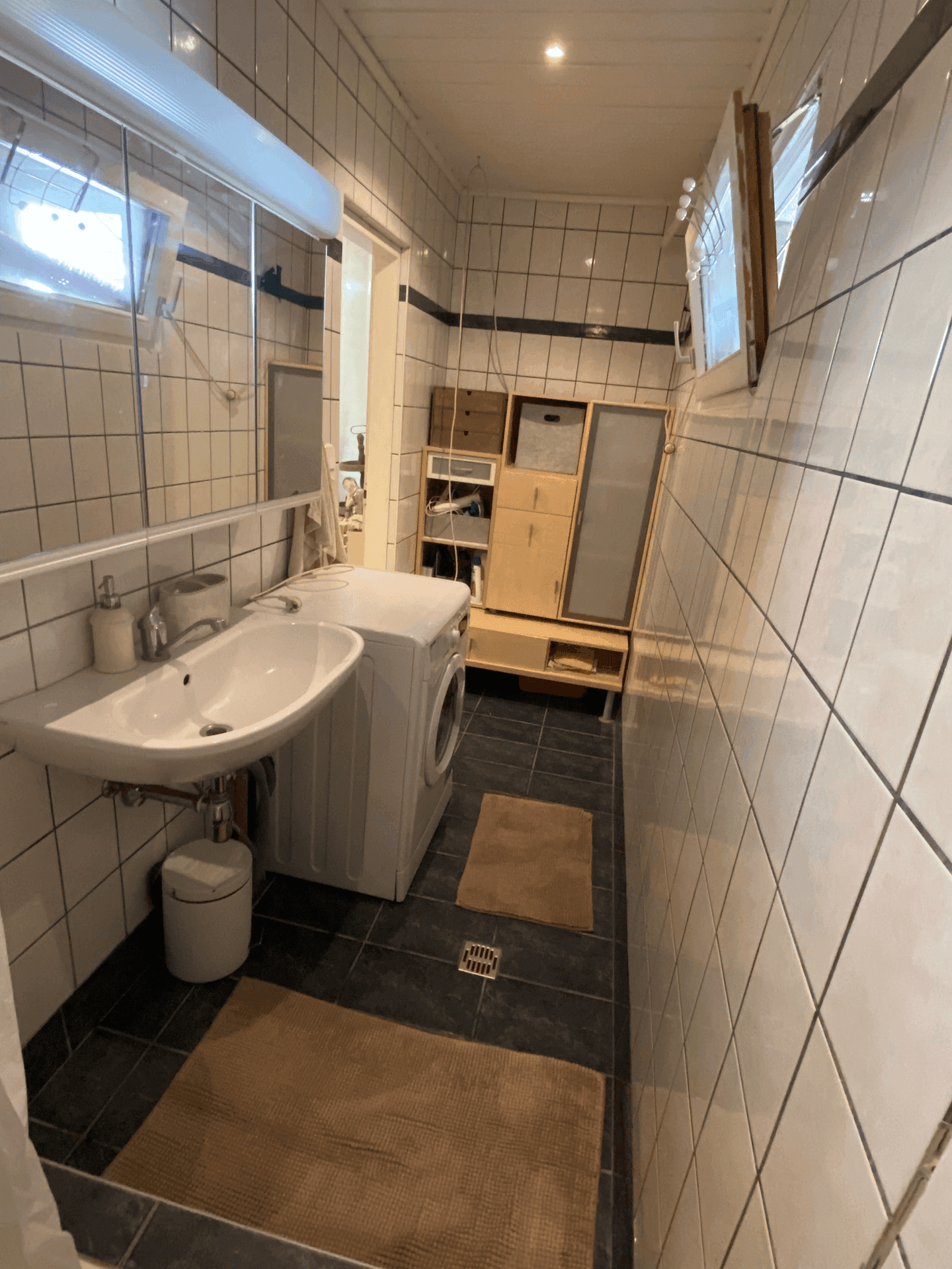 Funktionales Badezimmer mit Waschbecken, Waschmaschine und Spiegelschrank, hell gefliest.