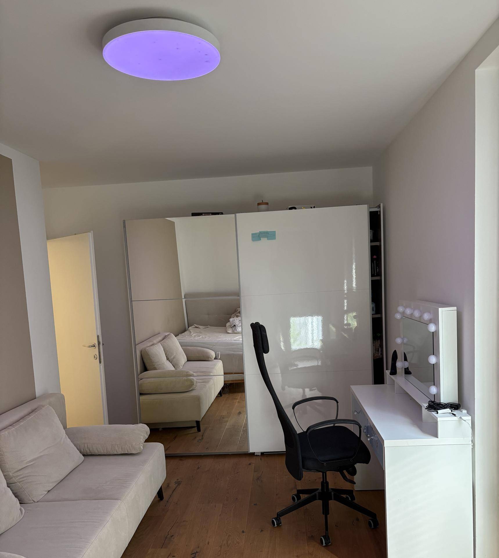 Helles Schlafzimmer mit Sofa, Spiegelschränken und Schminktisch.