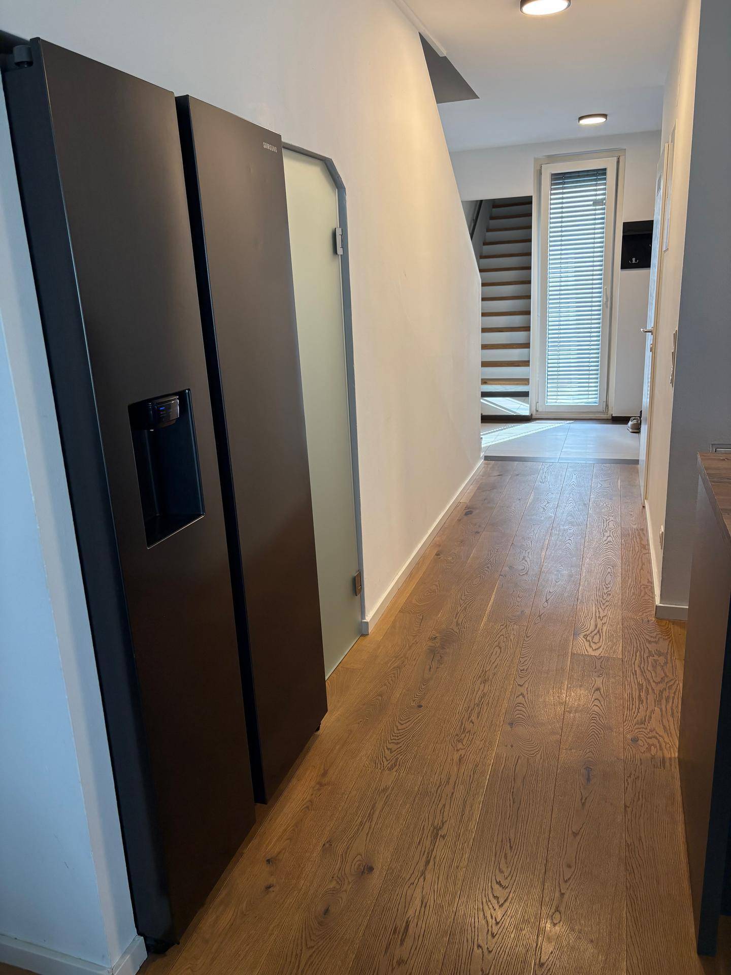 Langer Flur mit Holzboden, integriertem Kühlschrank und Blick zur Haustür.
