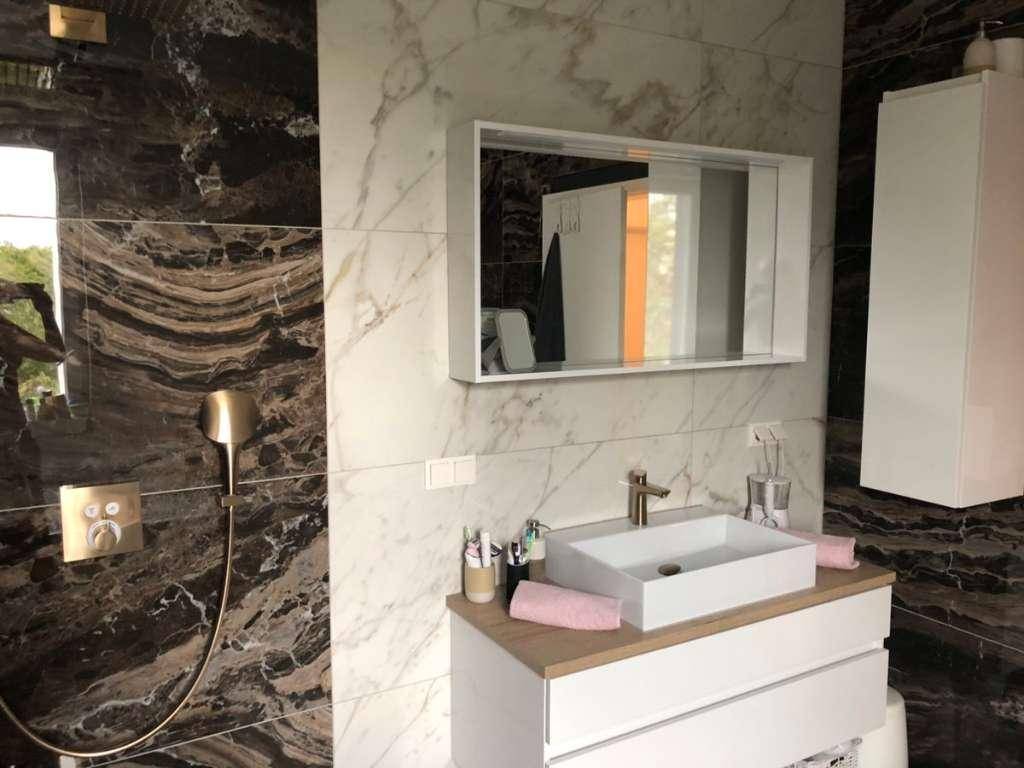Stilvolles Badezimmer mit Einzelwaschbecken, Spiegelschrank und dunklen Marmorfliesen an der Wand.