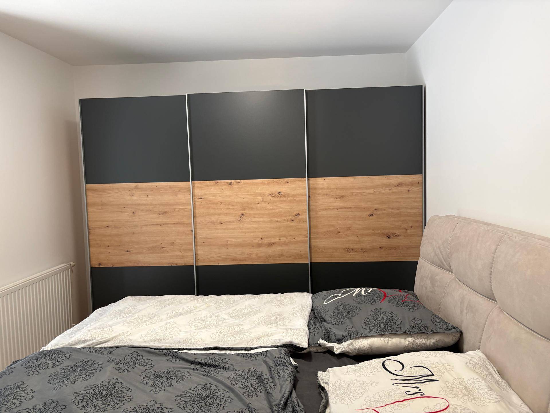 Schlafzimmer mit Doppelbett und modernem Kleiderschrank in Holz- und Anthrazitoptik.