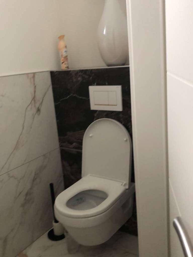 Modernes Gäste-WC mit wandhängender Toilette und eleganten Marmorfliesen an Wand und Boden.