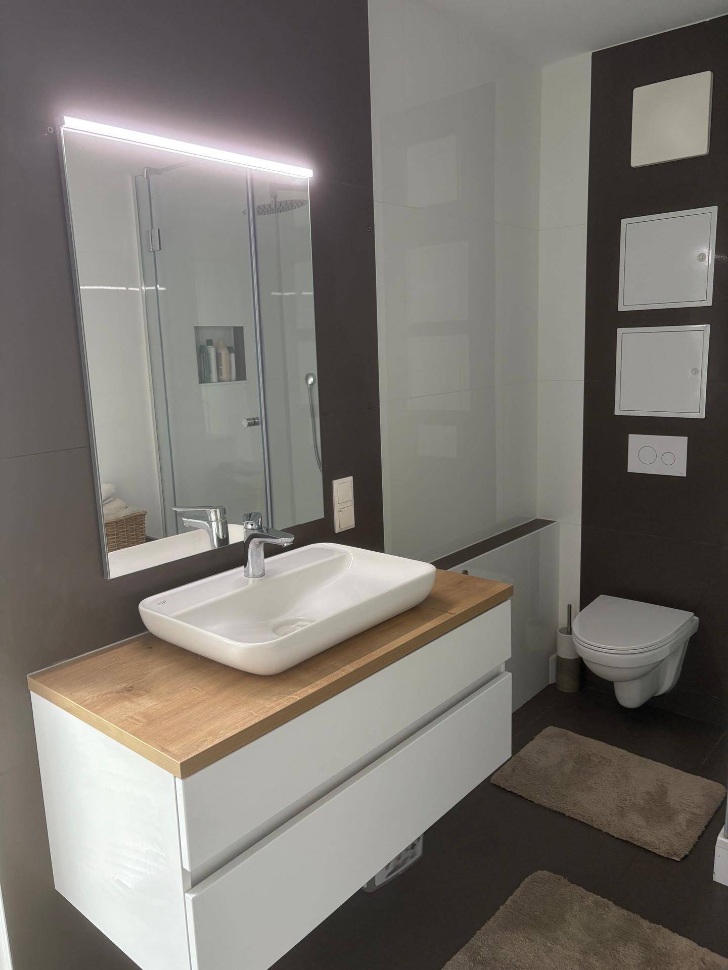Modernes Badezimmer mit Waschtisch, beleuchtetem Spiegel, Dusche und Wand-WC.