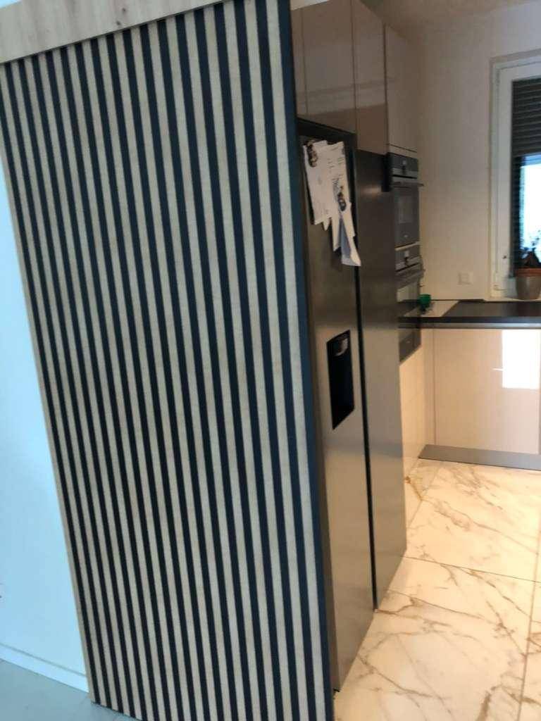 Küchenbereich mit modernem Kühlschrank und dekorativer Holzlamellenwand, die den Raum abgrenzt.