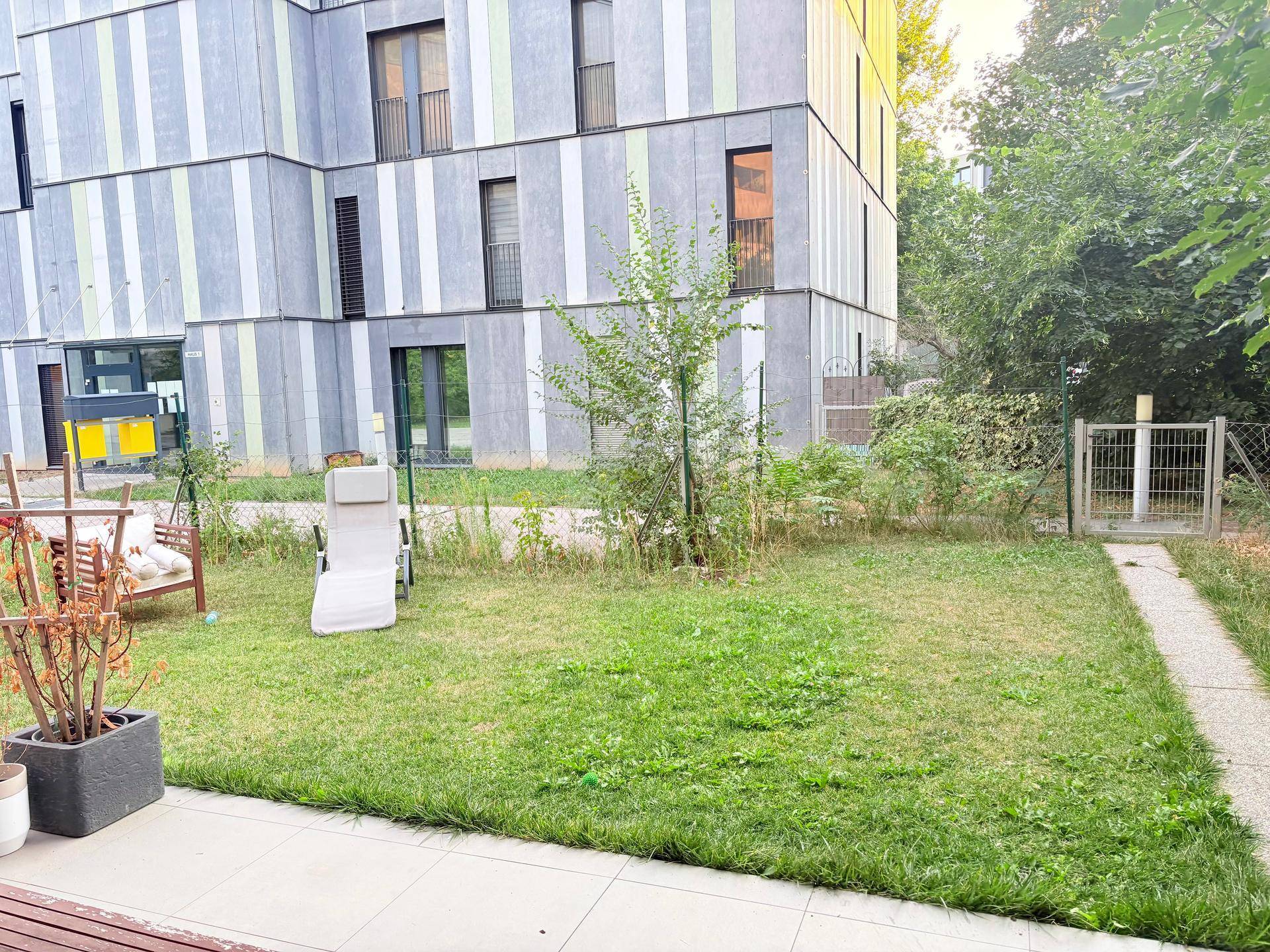 Kleiner Gartenbereich mit Rasenfläche, Liegestuhl und Blick auf das moderne Gebäude.